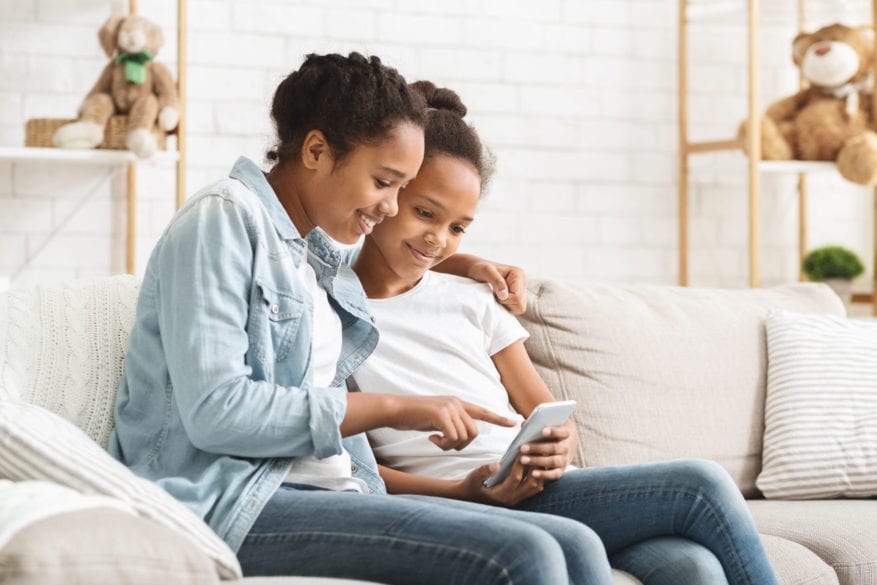 Two,Cute,African,American,Sisters,Using,Phone,On,Sofa,At - 92.5 The Beat